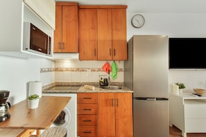 Eine Küche mit Holzausstattung, einem Edelstahlkühlschrank, einer Mikrowelle und einem Spülbecken.