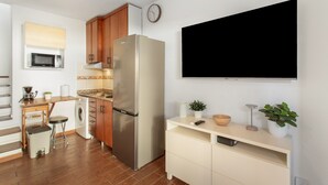 Una cocina compacta con un refrigerador de acero inoxidable, armarios de madera, un microondas, una lavadora y un televisor de pantalla plana montado en la pared.