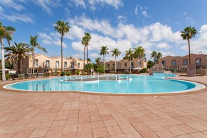 Ein Schwimmbecken mit Fliesenbord, umgeben von Palmen und Gebäuden im mediterranen Stil.