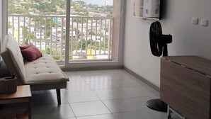 A modern living room with a sofa, a wooden cabinet, a TV mounted on the wall, and a large window offering a city view. - Apartment in Cartagena (Cartagena de Indias)