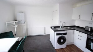 A compact kitchen with a washing machine, a sink, and a dining area with a chair.