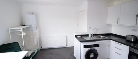 Una cocina compacta con lavadora, un lavamanos y una zona de comedor con una silla.