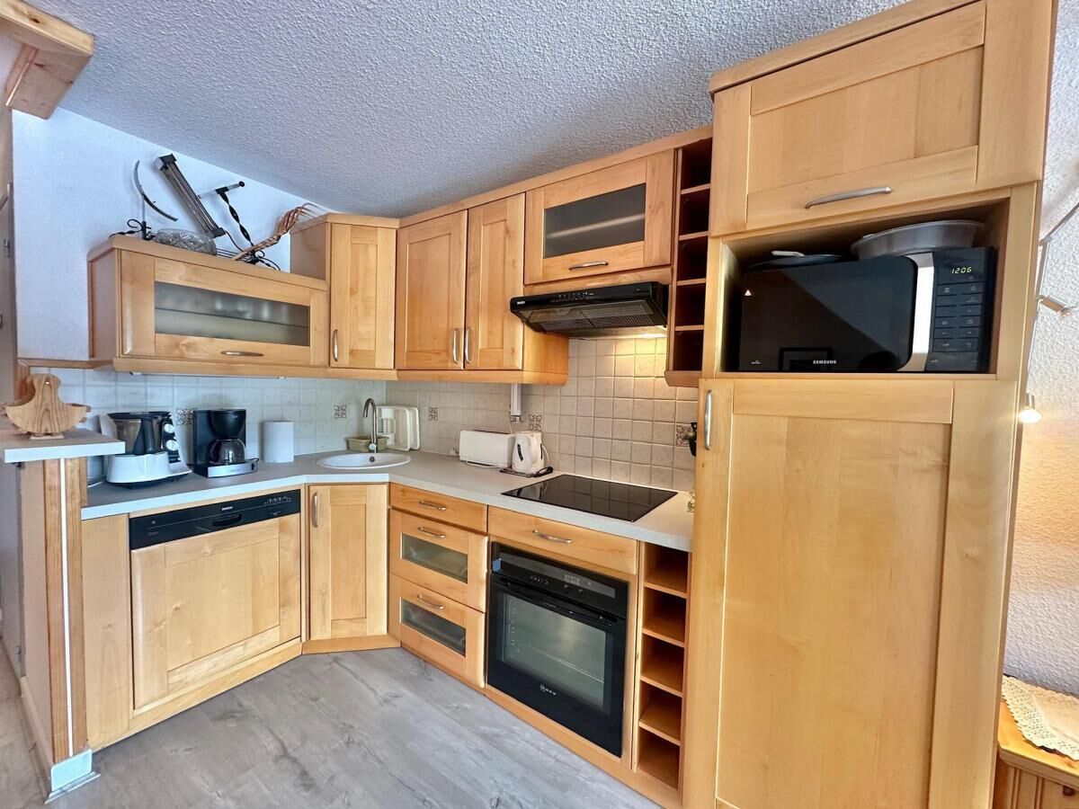 A compact kitchen with wooden cabinets, a built-in oven, a microwave, and a dishwasher.