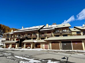 Un hôtel à plusieurs étages, doté de balcons et de portes en bois, avec une piste de ski en arrière-plan.