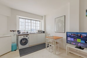 A compact kitchen with a washing machine, a microwave, and a dining area with a table and chair.