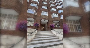 A brick building with a central entrance, multiple windows, and a staircase leading up to the entrance.