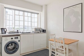 A compact kitchen with a washing machine, microwave, and a dining area with a table and chairs.