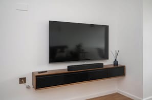 Ein Flachbildfernseher ist an einer Wand über einer Holzkonsole angebracht, zusammen mit einer Fernbedienung und einem kleinen dekorativen Gegenstand.