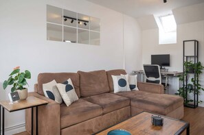 Ein Wohnzimmer mit braunem Sofa, einem kleinen Tisch, einem Fernseher und einer Pflanze.