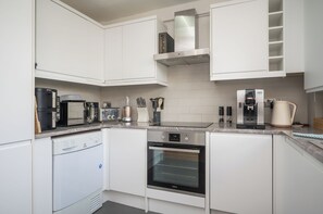 A modern kitchen with white cabinetry, a built-in oven, a coffee machine, and a kettle.