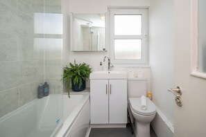 A bathroom with a bathtub, a sink, a toilet, and a window. - Sun Filled 1BD Split Level Flat by Caledonian Road (Greater London)