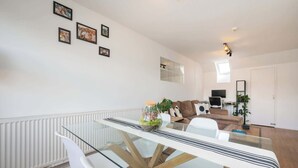 A modern living room with a glass dining table, white sofas, a TV, and a plant. - Sun Filled 1BD Split Level Flat by Caledonian Road (Greater London)