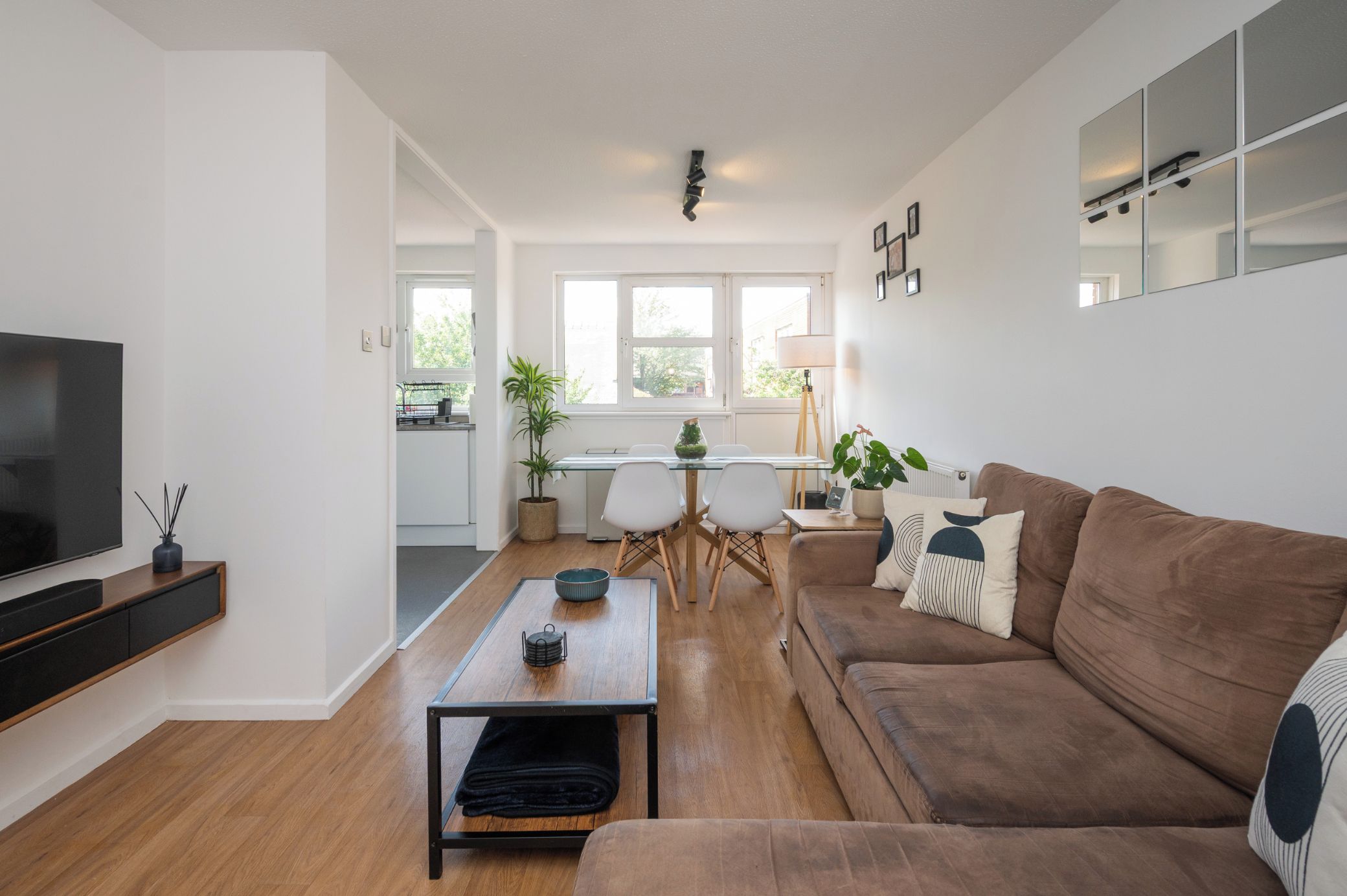 A modern living room with a brown sofa, a coffee table, a TV, and a dining area with a table and chairs.