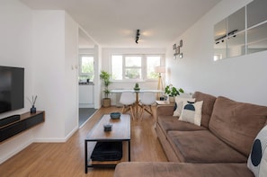 A modern living room with a brown sofa, a coffee table, a TV, and a dining area with a table and chairs.