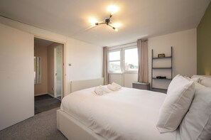 A hotel room with a large bed, a bedside table, a window with curtains, a radiator, and a ceiling light fixture. - Sun Filled 1BD Split Level Flat by Caledonian Road (Greater London)