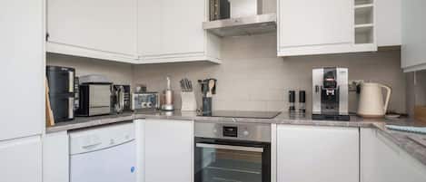 A modern kitchen with white cabinetry, a dishwasher, an oven, a coffee maker, and a kettle.