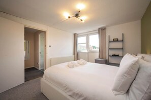 Un dormitorio de hotel con una cama grande, una mesita de noche, una ventana con cortinas, un radiador y una lámpara en el techo.