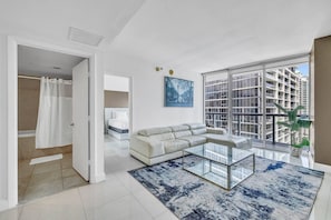A modern living room with a glass coffee table, a white sofa, and a large window with a city view.