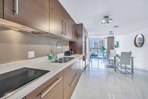 A modern kitchen with stainless steel appliances, wooden cabinets, and a dining area with a glass table and chairs.