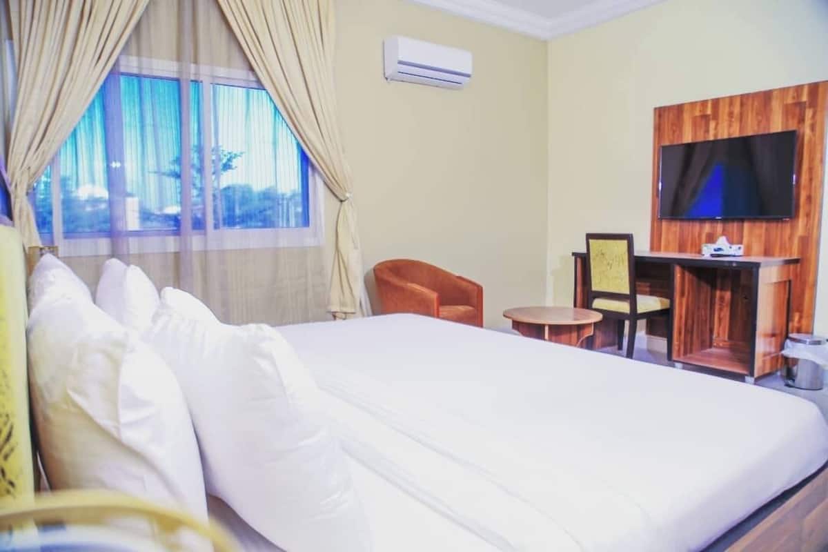 A hotel room with a large bed, a TV mounted on a wooden panel, a small table, and a chair.