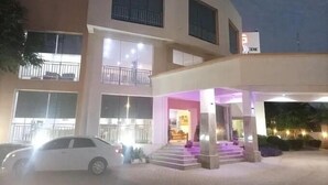 A multi-story hotel with a central entrance, a car parked in front, and a well-lit outdoor area. - De Guest Pride Hotel and Suites (Kano)