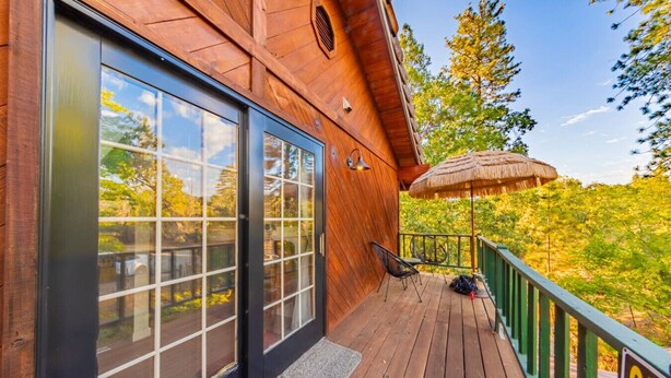 Une cabane en bois dotée de grandes portes coulissantes en verre, d’une terrasse avec un parasol en chaume et d’une rambarde verte.
