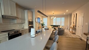 Una cocina moderna con una isla grande, electrodomésticos de acero inoxidable y un rincón comedor con un sofá gris.
