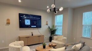 Una sala moderna con un televisor de pantalla plana montado en la pared, una consola de madera, un sofá gris y una mesa de centro redonda de madera.
