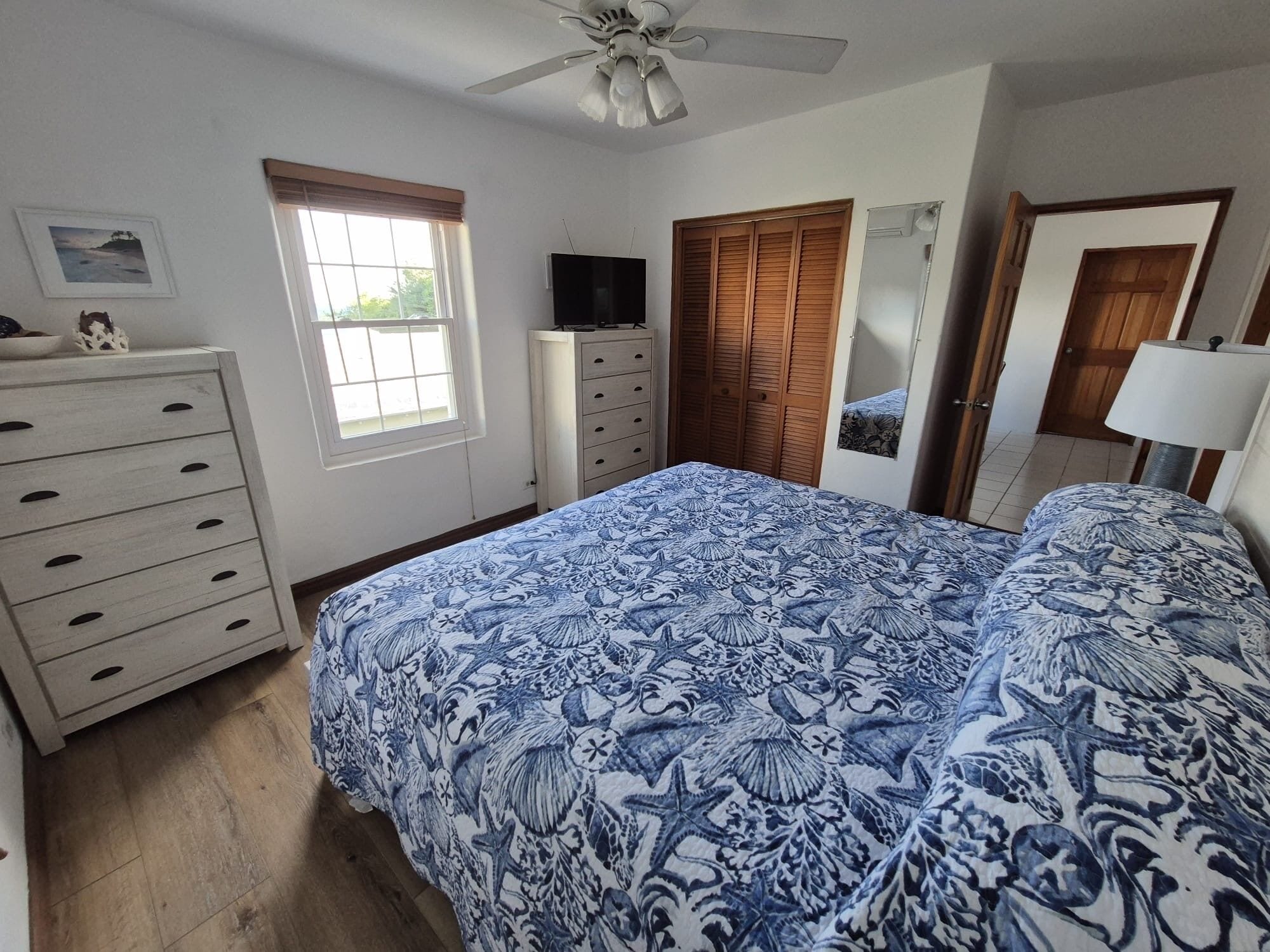 Ein Schlafzimmer mit Bett, Schminktisch, Fernseher, Kleiderschrank und Deckenventilator.