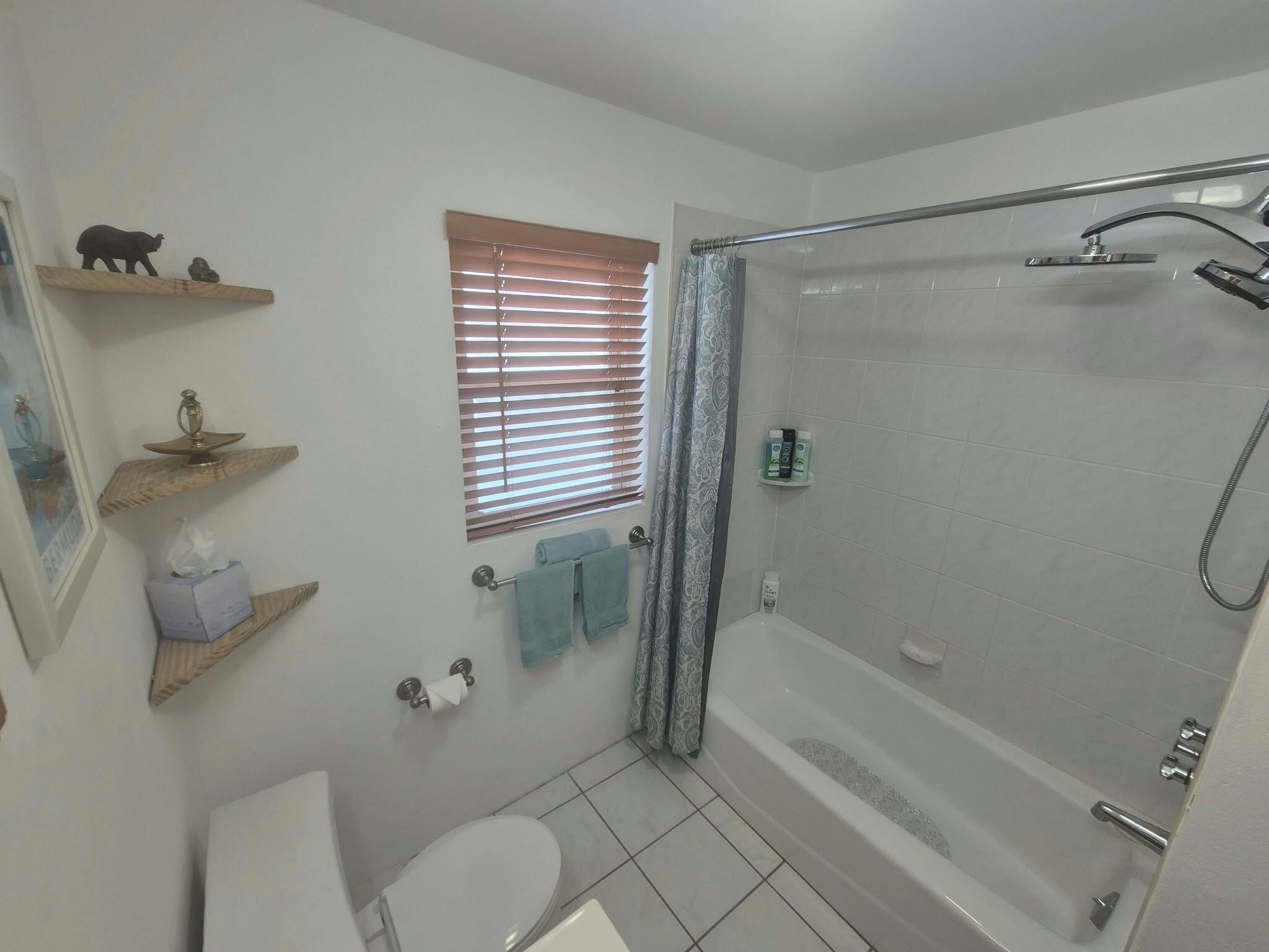 A bathroom with a bathtub, toilet, and a window with blinds.