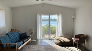 Amplia sala de estar con un ventanal que ofrece vistas al mar, un ventilador de techo, un sofá, una silla y una mesita.