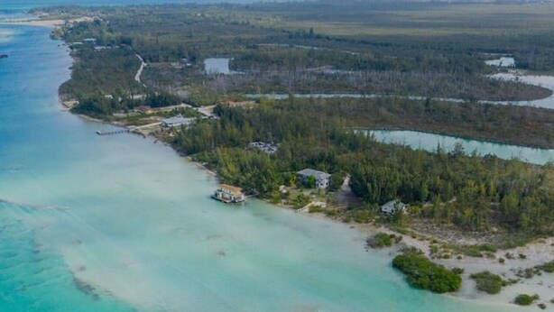 Vista aérea de una propiedad costera con un mar turquesa cristalino, una pequeña playa y zonas boscosas.