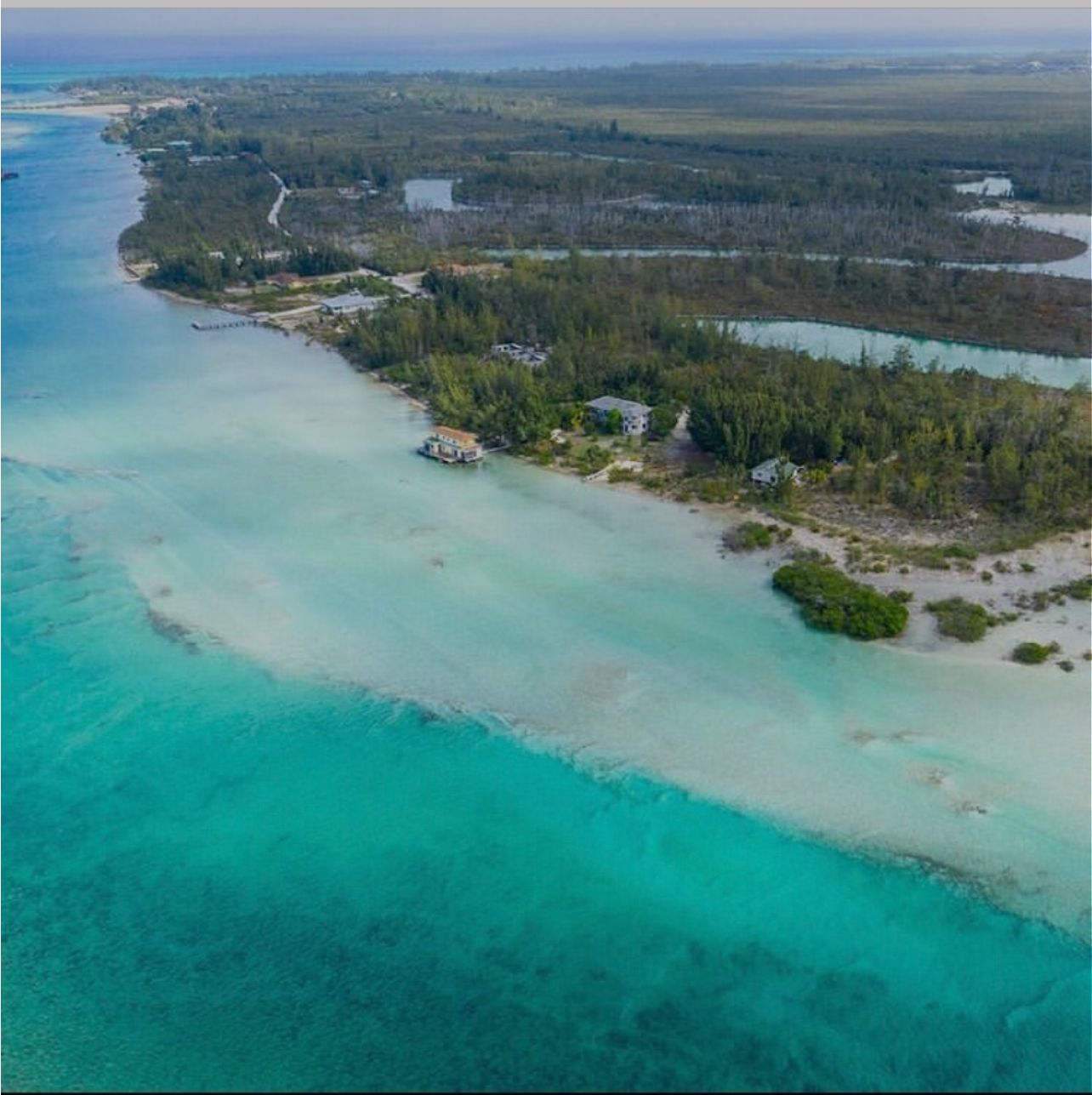 Vista aérea de una propiedad costera con un mar turquesa cristalino, una pequeña playa y zonas boscosas.