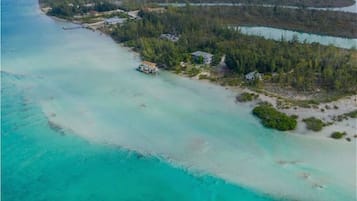 Vista aérea de una propiedad costera con un mar turquesa cristalino, una pequeña playa y zonas boscosas.