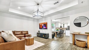 Een moderne woonkamer met een bruine leren bank, een houten salontafel en een flatscreen televisie aan de muur.
