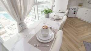 A modern kitchen with white cabinets, a marble countertop, and a dining area with a table set for two.