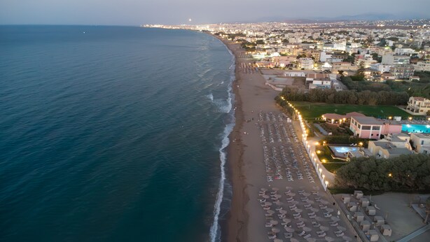 Vista aérea de una ciudad costera con una playa bordeada por sillas de sol y sombrillas.