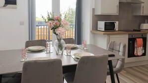A dining area with a table set for four, a vase with flowers, and a kitchen with a microwave and oven.