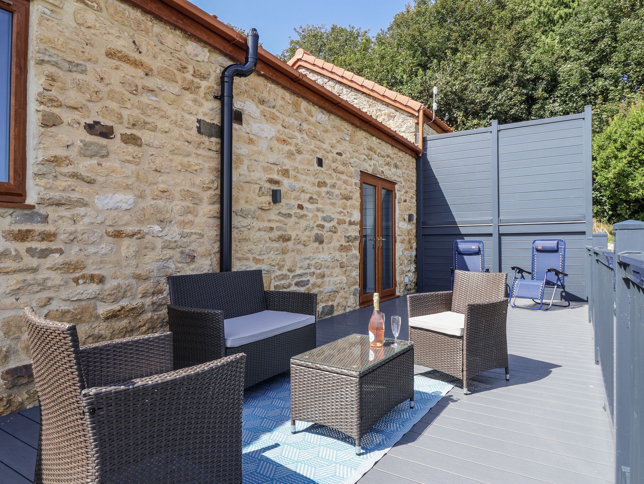 A stone building with outdoor wicker furniture and a glass table.