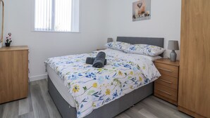 A bedroom with a bed, a bedside table, a dresser, a window with blinds, and a wall decoration.