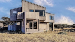 Une maison moderne à deux étages, dotée de grandes fenêtres et d’un toit plat, située dans un champ verdoyant.