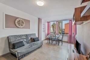 A living area with a sofa, dining table, chairs, and a TV.