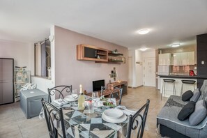 A modern kitchen with bar stools, a dining table set for two, and a sofa in the living area.