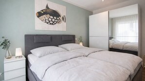 A bedroom with a large bed, a nightstand, a lamp, a mirror, and a wall art of a fish. - Your exclusive penthouse in a perfect location - pure luxury and relaxation with its own (Norderney)