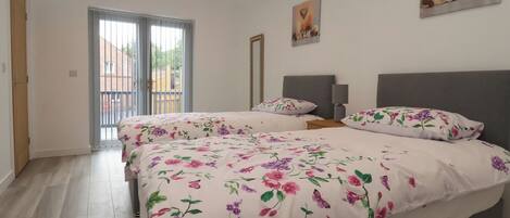 A bedroom with two beds, a large window, and a balcony.