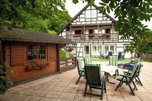 A traditional wooden house with a balcony, a patio with outdoor furniture, and a garden area. - Vacation apartment An der Lenne (Schmallenberg)