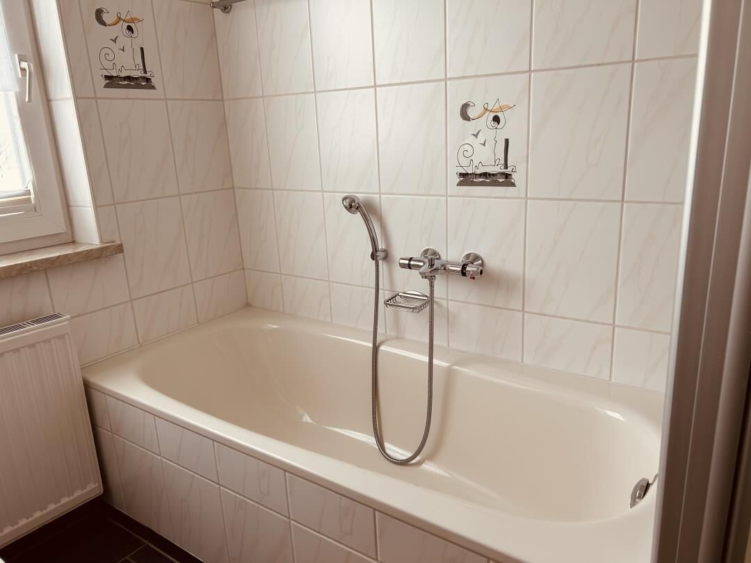 Un baño con una bañera blanca, un cabezal de ducha y azulejos decorativos.