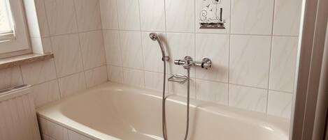 Un baño con una bañera blanca, un cabezal de ducha y azulejos decorativos.