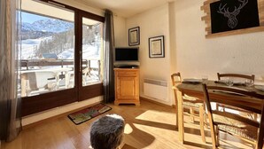 A cozy room with a wooden dining table, chairs, a television, and a large window offering a view of a snowy landscape.
