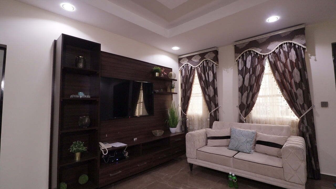 A living room with a beige sofa, dark wooden entertainment unit, and curtains.